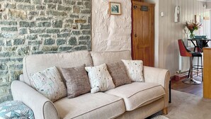 A beige sofa with floral cushions, a stone wall, and a wooden door in a cozy room. - The Old Post House Annex - UK50190 (Axbridge, near Weare)