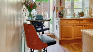 A kitchen with wooden cabinets, a washing machine, and a dining area with a table and chairs. - The Old Post House Annex - UK50190 (Axbridge, near Weare)