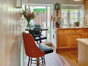 A kitchen with wooden cabinets, a washing machine, and a dining area with a table and chairs. - The Old Post House Annex - UK50190 (Axbridge, near Weare)