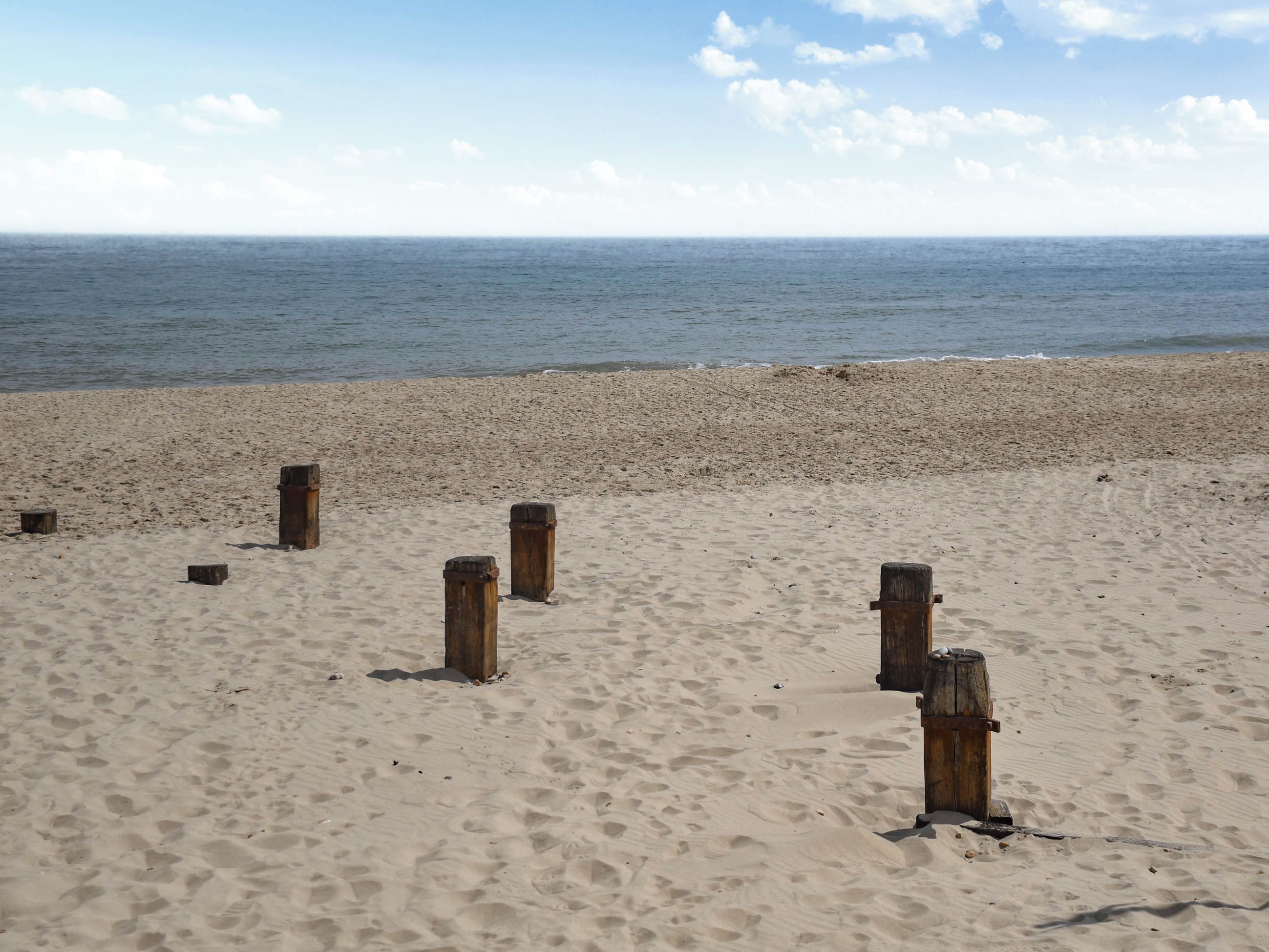 A sandy beach with wooden posts and the ocean in the background.
