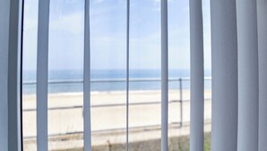 A view through a window with vertical blinds, overlooking a beach with a sandy shore and a calm sea. - This seaside retreat blends modern comfort with spectacular sea views. (Bacton)