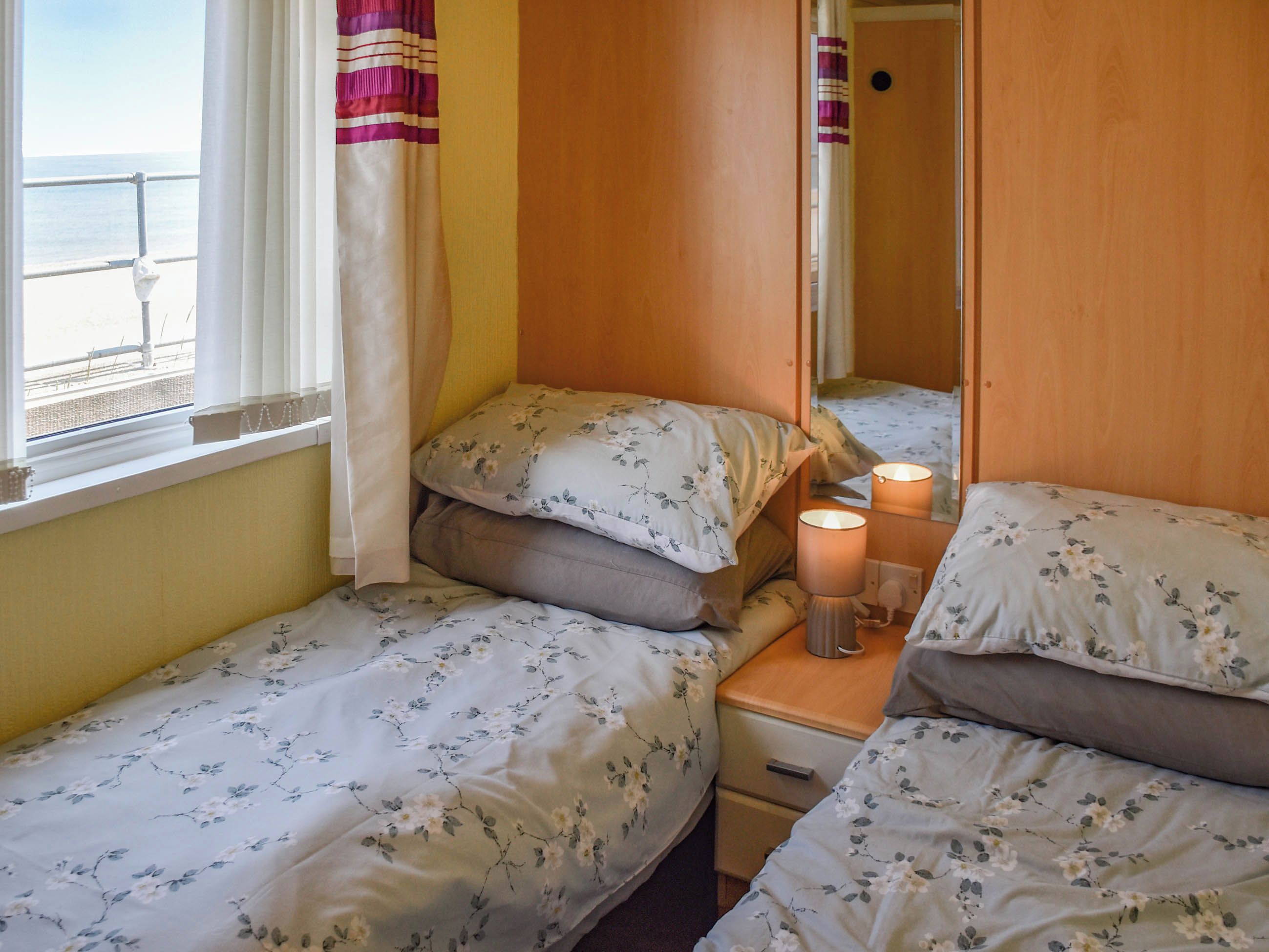 Habitación con dos camas, cada una con ropa de cama estampada, una mesita de noche con lámpara y una ventana con cortinas.