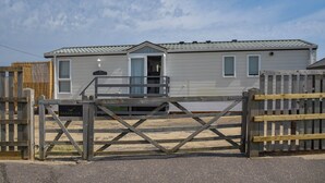 A single-story mobile home with a front porch and a gated entrance. - This seaside retreat blends modern comfort with spectacular sea views. (Bacton)