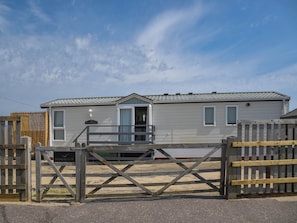 Une maison mobile de plain-pied, dotée d’un porche à l’avant et d’une entrée fermée par un portail.