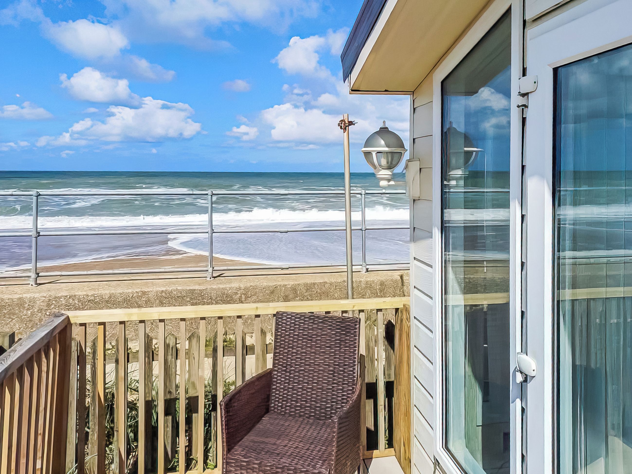 Een balkon met uitzicht op strand en zee, een lantaarnpaal en een houten omheining.