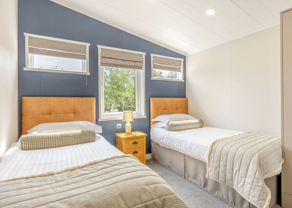 A bedroom with two beds, a window, and a nightstand with a lamp.