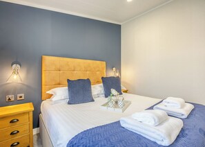 A hotel room with a bed, bedside tables, a nightstand, a lamp, and a tray with toiletries.