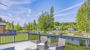 A deck with wicker furniture and a view of a lake. - Monument Lakeside Lodge Pet Friendly (Woodhall Spa)