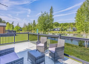 A deck with wicker furniture and a view of a lake. - Monument Lakeside Lodge Pet Friendly (Woodhall Spa)