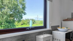 Una cocina con ventana, tetera, panera y microondas.