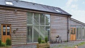 Una casa de madera con un ventanal grande, una puerta y un pequeño jardín con gallinas.