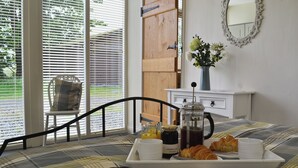 Una bandeja de desayuno con cruasanes, café y jugo sobre una cama con una manta escocesa. Una silla y un tocador con espejo se ven al fondo.