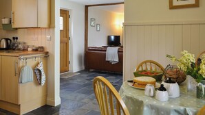 Una cocina con armarios de madera, una mesa de comedor con mantel de lunares y un televisor al fondo.