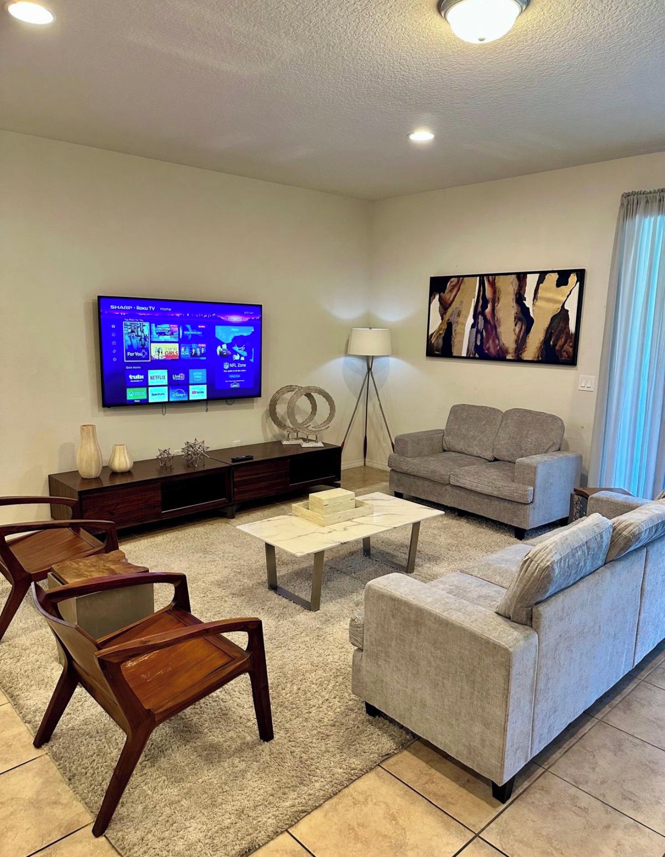 A living room with a flat-screen TV, a grey sofa, a coffee table, and a wooden chair.