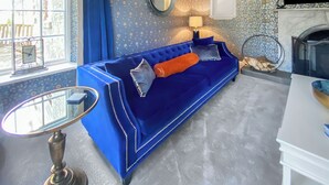 Ein Zimmer mit einem blauen Sofa, einem runden Spiegel, einem Kamin und einem Fenster mit Vorhängen.