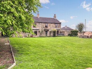 A stone house with a well-maintained lawn and a large tree in the foreground.