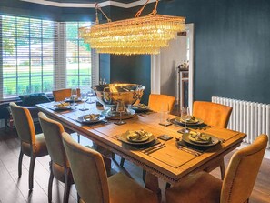 Une salle à manger avec une grande table en bois dressée pour un repas, entourée de chaises, et un lustre suspendu au plafond.