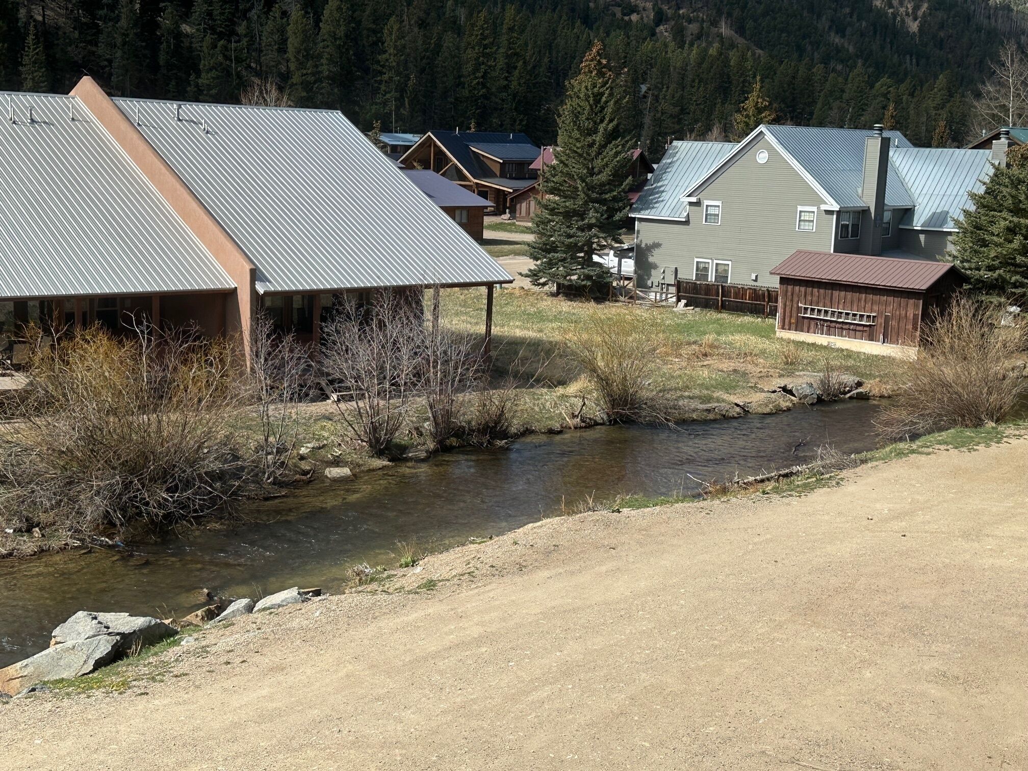 A rural setting with a river, wooden cabins, and a mountain backdrop.