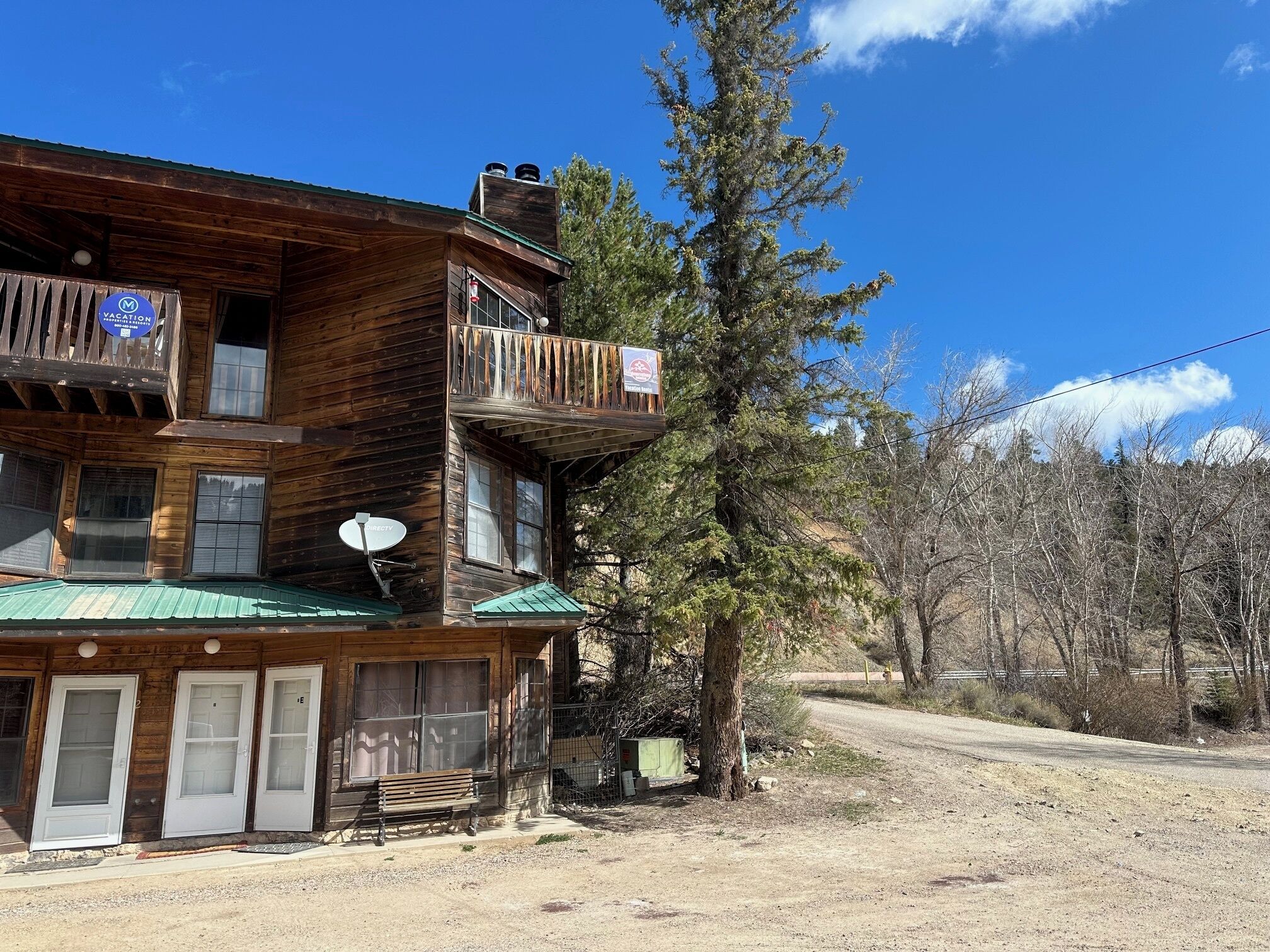 A wooden cabin with a balcony, a satellite dish, and a green roof.