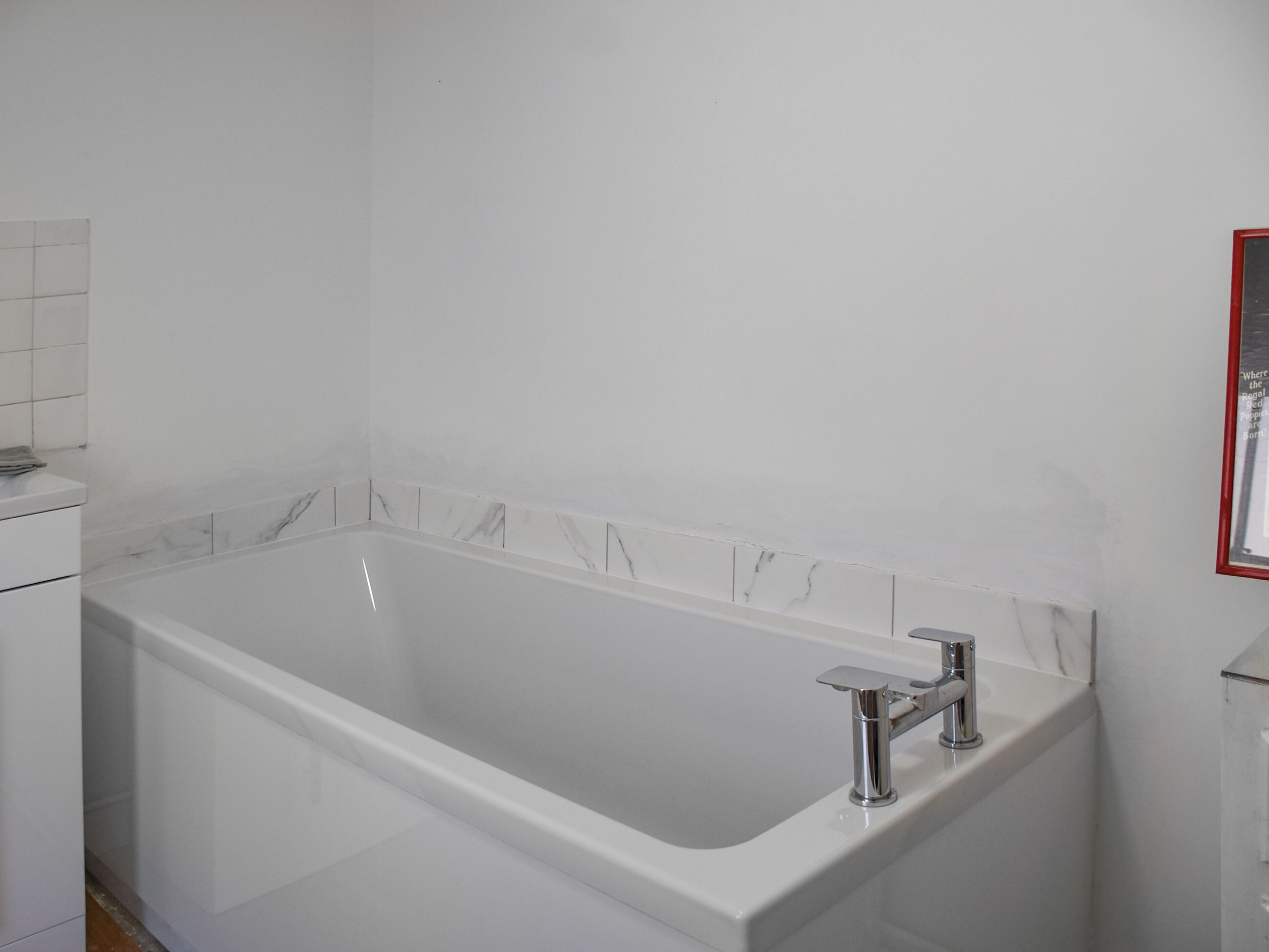 Une salle de bain moderne avec une baignoire blanche, des robinetteries chromées et des carreaux à motifs de marbre.