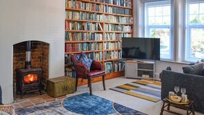 A cozy living room with a fireplace, a bookshelf, a television, and comfortable seating. - 2 bedroom accommodation in Cromer (Cromer)