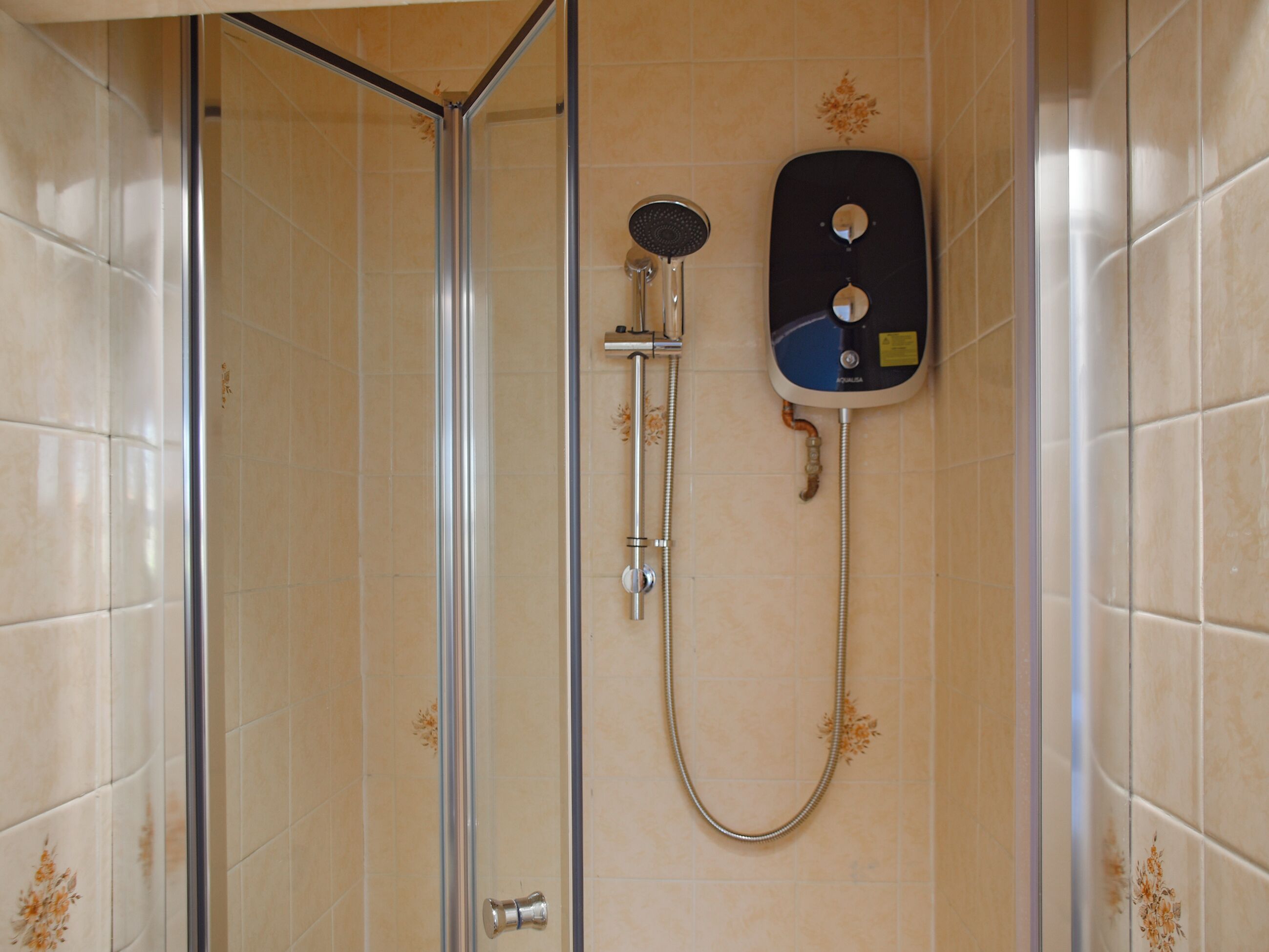Une cabine de douche équipée d’un pommeau de douche à main et d’un panneau de commande fixé au mur.