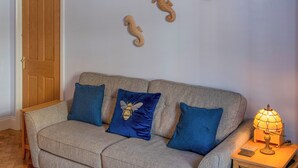 En stue med en beige sofa, to blå puder, et træsidebord med en lampe og tre vægdekorationer med hestehale.