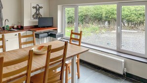 Een moderne keuken met een eethoek, een televisie en een groot raam met uitzicht op een tuin.