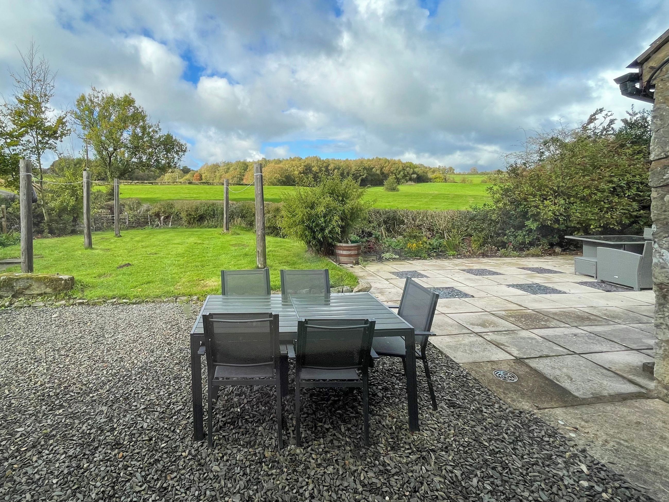 Eine Terrassengruppe mit Tisch und Stühlen, umgeben von Kies, mit Blick auf ein grünes Feld und Bäume im Hintergrund.