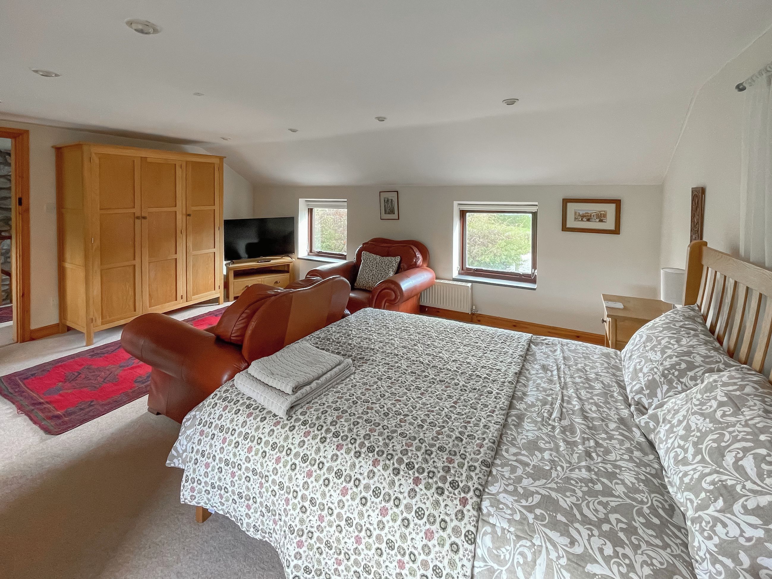 Een slaapkamer met een groot bed, een houten garderobe, een televisie en een raam.