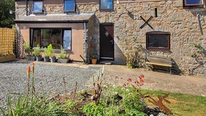 Een twee verdiepingen tellend stenen huis met veel ramen, een voordeur en een kleine tuin met planten en bloemen in potten.