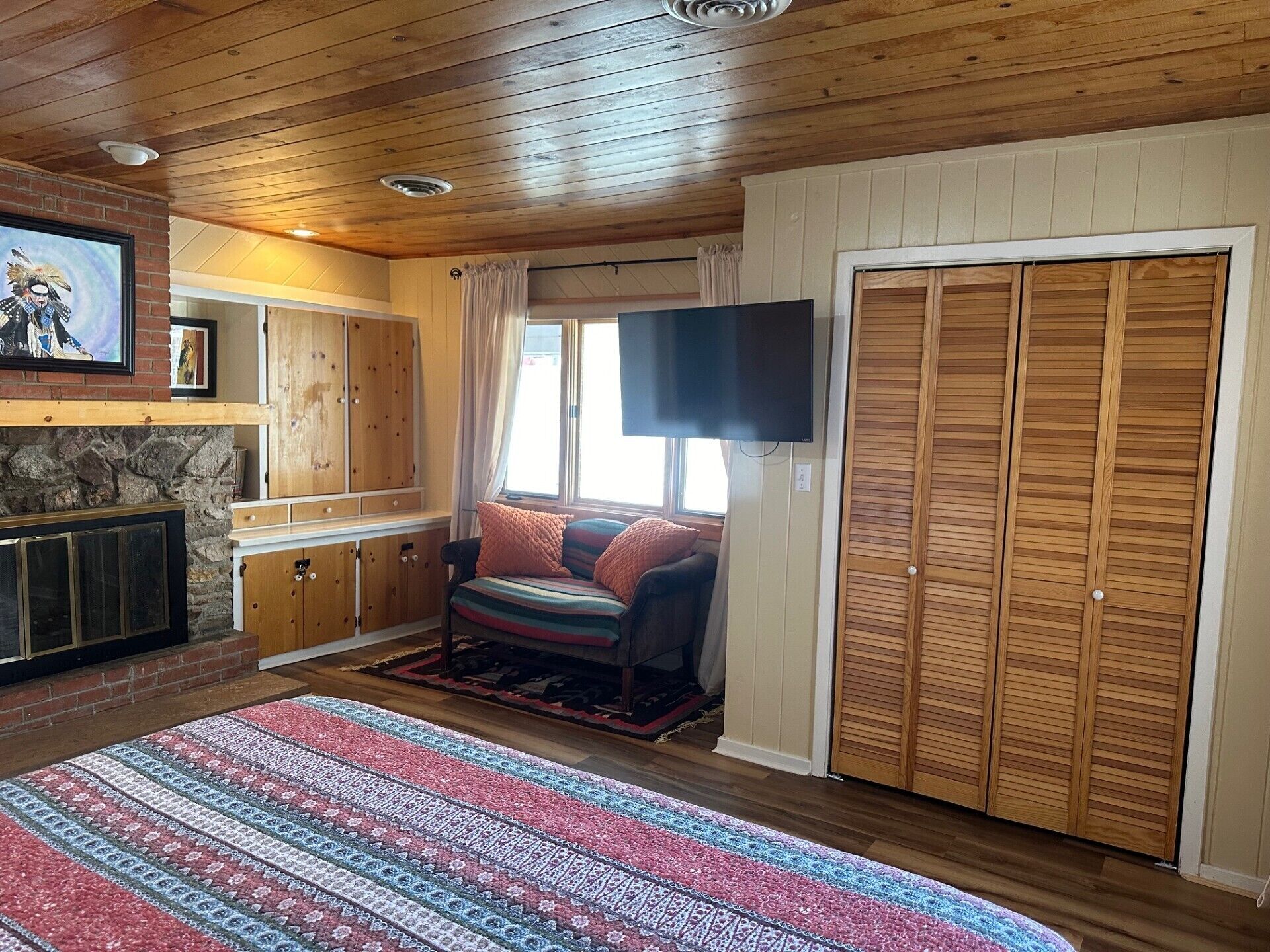 Una habitación acogedora con chimenea, armarios de madera, televisión y un gran ventanal.