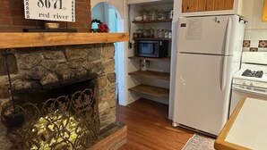 A kitchen with a stone fireplace, wooden cabinets, a white refrigerator, and a stove. - Collettes on Mallette (Red River)