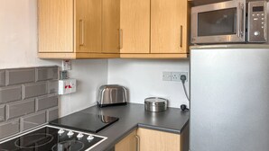 A modern kitchen with wooden cabinets, a stainless steel microwave, a toaster, and a gas stove.