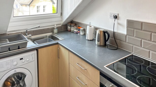 A compact kitchen with a washing machine, a kettle, and a sink.