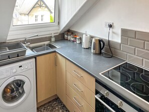 A compact kitchen with a washing machine, a kettle, and a sink.