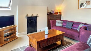 A living room with a TV, wooden entertainment unit, a fireplace, a sofa, and a lamp.