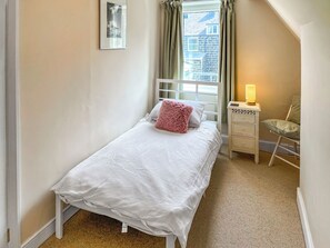 Un dormitorio pequeño y ordenado con una cama individual, una mesita de noche con lámpara y una silla.