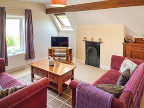 A cozy living room with a wooden coffee table, red sofas, a fireplace, and a television on a wooden stand.