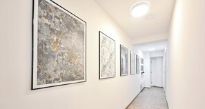 Un couloir aux murs ornés d’œuvres d’art abstraites encadrées, une porte blanche au fond et un luminaire au plafond.