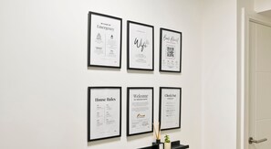 Framed documents on a wall, including emergency services, WiFi, house rules, and a welcome message.