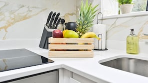 A kitchen with a marble backsplash, a fruit basket, a knife block, a bottle of hand wash soap, and a potted plant.