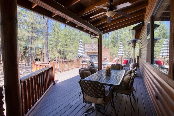 A covered outdoor deck with a table and chairs, a ceiling fan, and a view of trees.