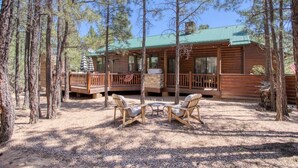 Une cabane avec une terrasse, deux chaises et une table, située dans une forêt.