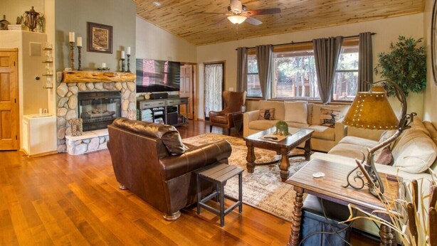 Un salon chaleureux avec une cheminée en pierre, un canapé en cuir, une table basse en bois et un ventilateur de plafond.