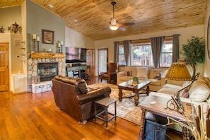 A cozy living room with a stone fireplace, leather sofa, wooden coffee table, and a ceiling fan.