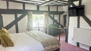 Un dormitorio con cama, ventana con cortinas, radiador y televisor montado en la pared.
