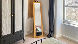 A bedroom with a bed, a wardrobe, a mirror, a window with a stone wall view, and a wooden door. - 3 bedroom accommodation in St Ives (St Ives)