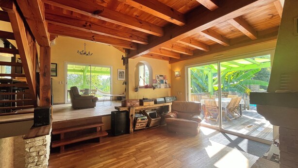 A spacious living area with a wooden ceiling, a stone fireplace, and a large sliding glass door leading to an outdoor patio with a hammock and dining area. - In the countryside near the beach (Saint-Barthelemy)