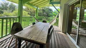 A wooden table and chairs on a porch with a green railing, overlooking a garden with trees and a hammock. - In the countryside near the beach (Saint-Barthelemy)